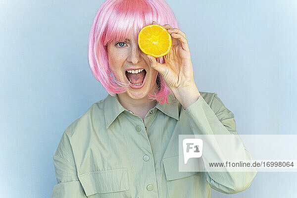 Porträt einer unbekümmerten jungen Frau mit rosa Perücke  die eine Orange hält