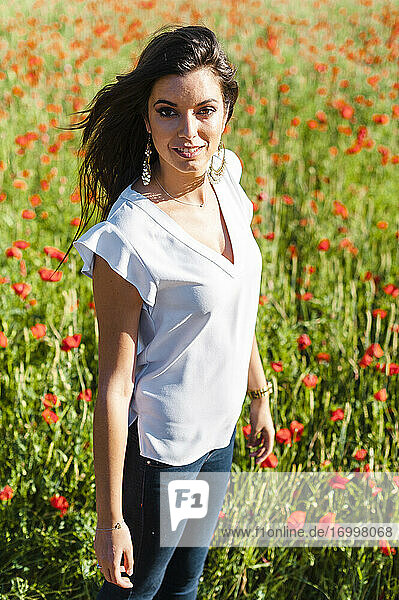 Smiling beautiful woman standing at poppy field during springtime