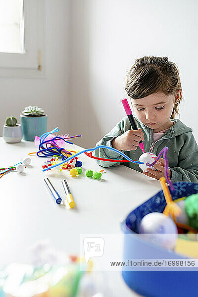 Mädchen lernt  kreatives Spielzeug aus Pfeifenreinigern und Styroporkugeln am Tisch an der Wand herzustellen