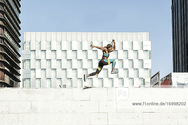 Young female athlete running on wall in city