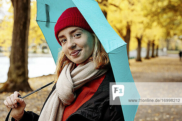 Schönes Teenager-Mädchen hält Regenschirm  während sie im Park steht