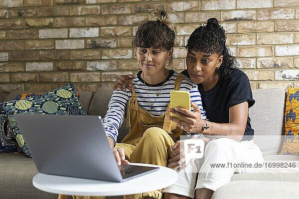 Frau  die einen Laptop benutzt  während ihre Freundin zu Hause ein Mobiltelefon benutzt