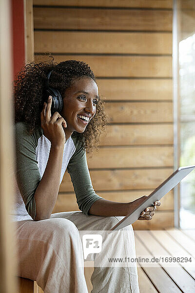 Lächelnde Frau  die über Kopfhörer spricht  während sie zu Hause ein digitales Tablet benutzt