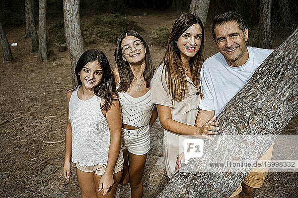 Lächelnde Familie steht hinter einem Baumstamm im Wald