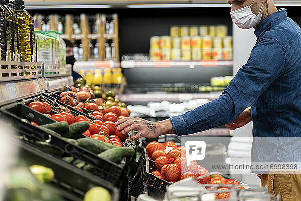 Mittelteil eines Mannes mit Gesichtsmaske beim Kauf von Gemüse im Supermarkt