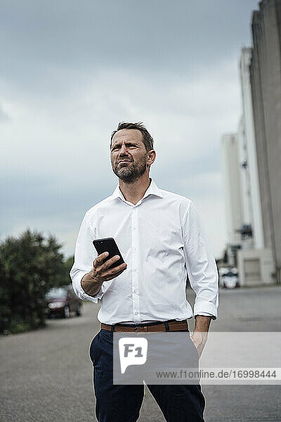Männlicher Unternehmer  der ein Smartphone hält  während er auf der Straße steht