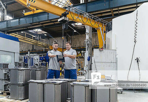 Männliche Angestellte beim Brainstorming  während sie an einer Maschine in einer Fabrik stehen