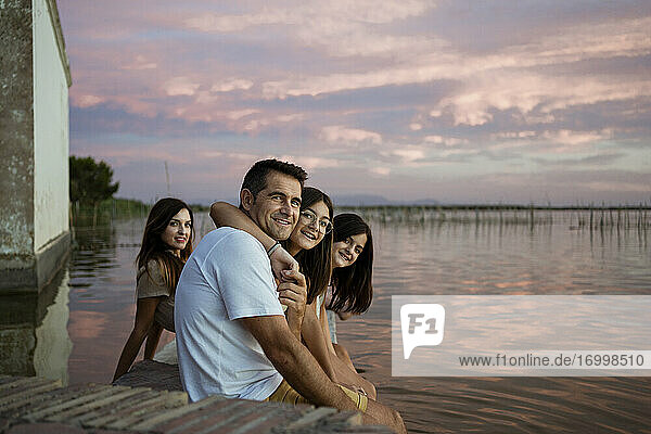 Lächelnde Familie sitzt bei Sonnenuntergang auf einer Stützmauer