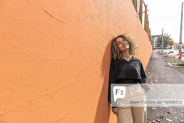 Lächelnde Frau mit Hand in der Tasche an die Wand gelehnt