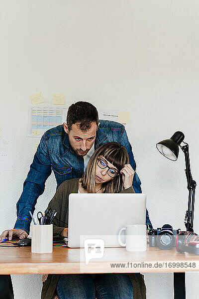 Freiberufliche Geschäftsfrau  die an einem Laptop arbeitet  während ein männlicher Kollege das Büro zu Hause betrachtet