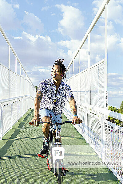 Mann hört Musik beim Fahrradfahren auf einer Brücke