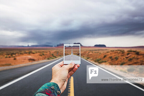 USA  Utah  Hand  die ein Sofortfoto über der Straße zum Monument Valley hält