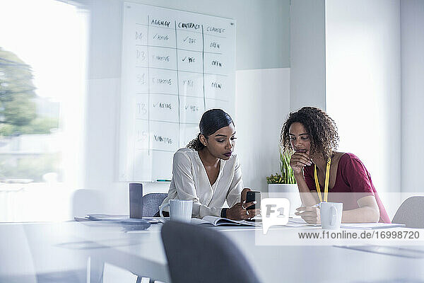 Weibliche Kollegen benutzen ihr Smartphone  während sie am Schreibtisch im Büro sitzen