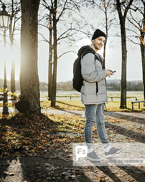 Mann hält Smartphone während eines Herbstspaziergangs im Park