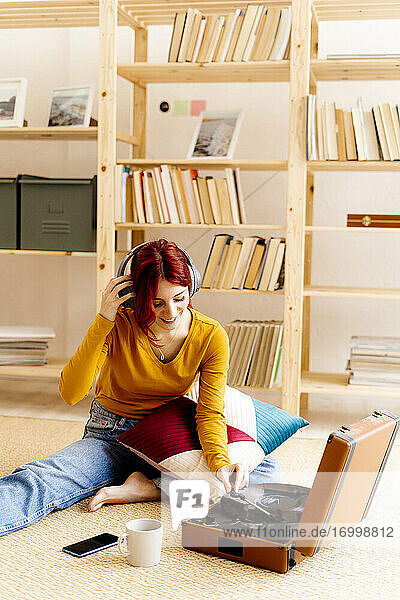 Smiling woman wearing headphones while using turntable sitting at home