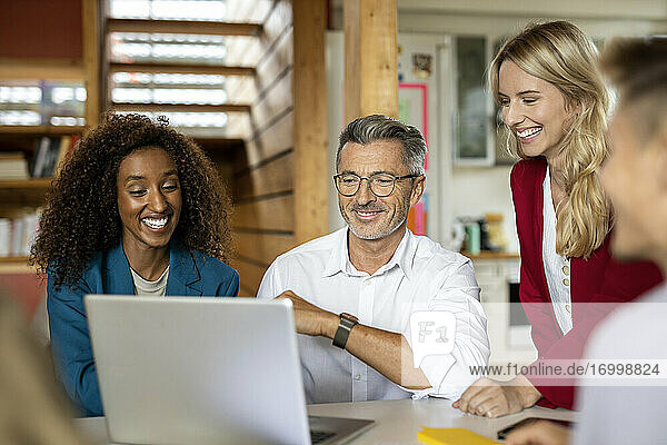 Lächelnde Geschäftsleute  die einen Laptop benutzen  während sie in einer Besprechung im Büro zusammenarbeiten