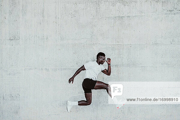 Young male athlete jumping by white wall