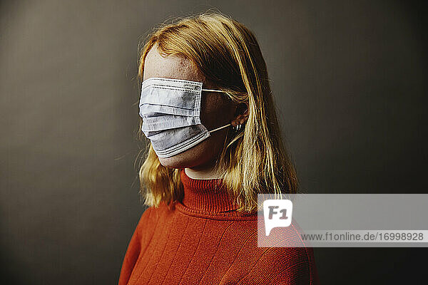 Blondes Mädchen trägt eine Schutzmaske auf dem Gesicht und steht vor einem grauen Hintergrund