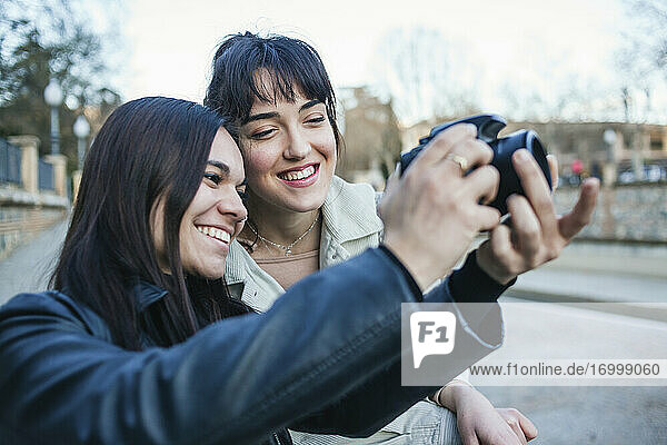 Lächelnde Frau  die neben ihrer Freundin steht und mit einer DSLR-Kamera fotografiert