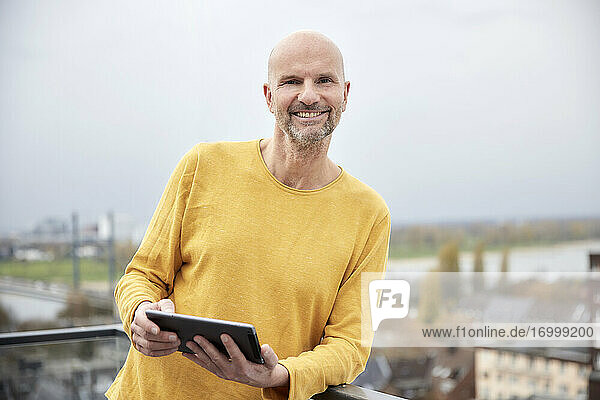 Mann mit digitalem Tablet  der lächelnd auf einem Dach steht