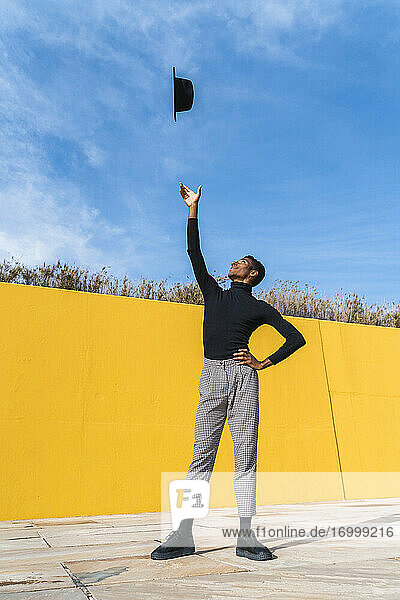 Junger Mann mit schwarzem Hut  tanzend vor einer gelben Wand