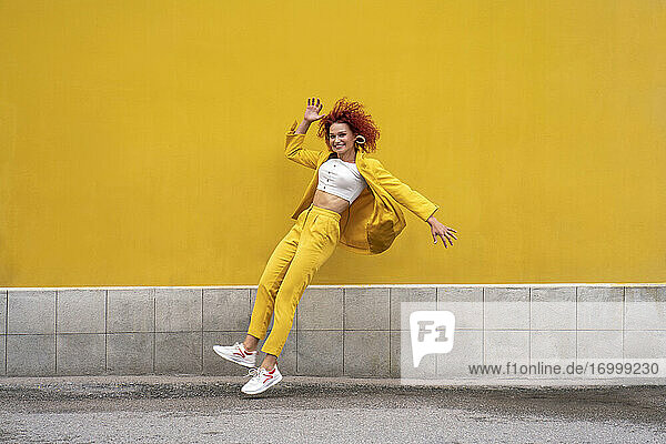 Energetische junge Frau in gelbem Anzug läuft und springt vor einer gelben Wand