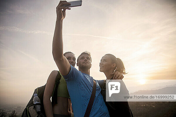 Lächelnde Freunde nehmen Selfie durch Handy  während gegen den Himmel stehen