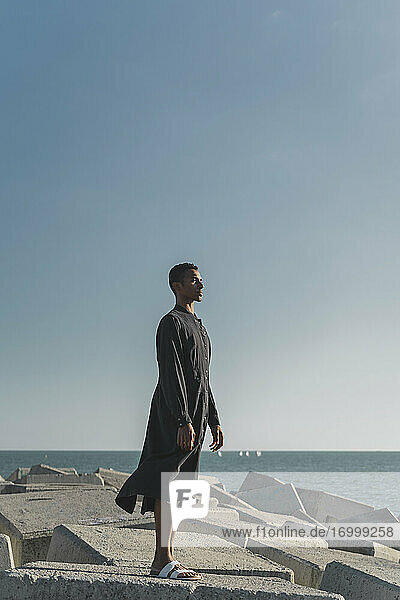 Junger Mann steht an der Küste und trägt einen schwarzen Kaftan