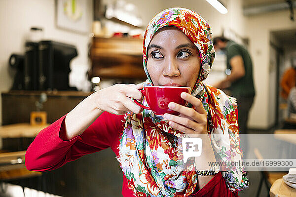 Malaysian woman looking away while drinking coffee in cafe