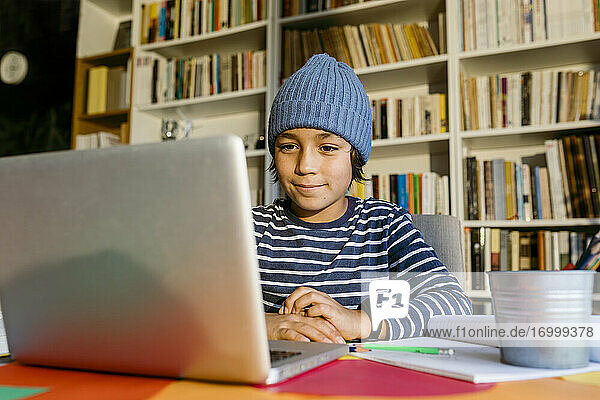 Junge  der über einen Laptop am Wohnzimmertisch am Hausunterricht teilnimmt