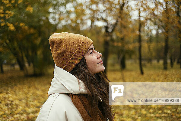 Smiling young woman day dreaming in autumn park