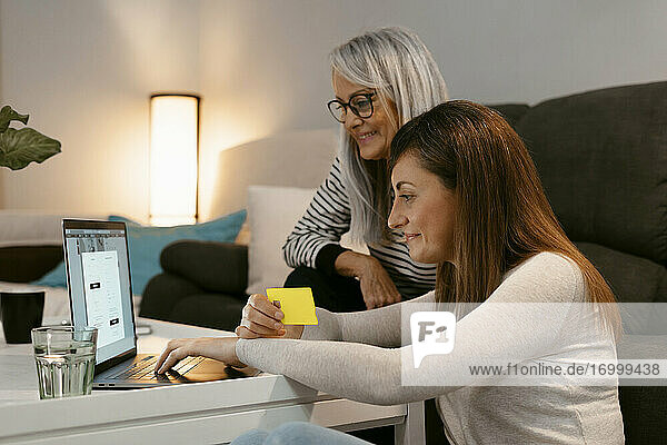 Smiling mother and daughter doing online shopping on laptop while sitting at home