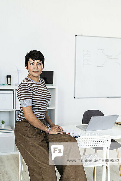 Porträt einer Geschäftsfrau  die am Rand eines Bürotisches sitzt