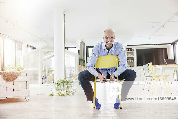 Lächelnder Geschäftsmann  der ein digitales Tablet benutzt  während er auf einem Stuhl im Büro zu Hause sitzt