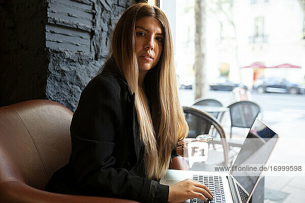 Junge Frau hält eine Brille und benutzt einen Laptop im Café