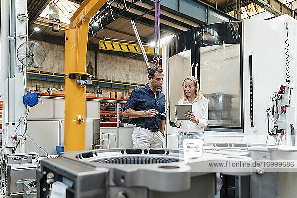 Geschäftsfrau  die ein digitales Tablet benutzt  während ein männlicher Kollege in einer Fabrik daneben steht