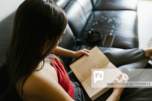 Teenager-Mädchen liest ein Buch  während sie zu Hause auf dem Sofa sitzt