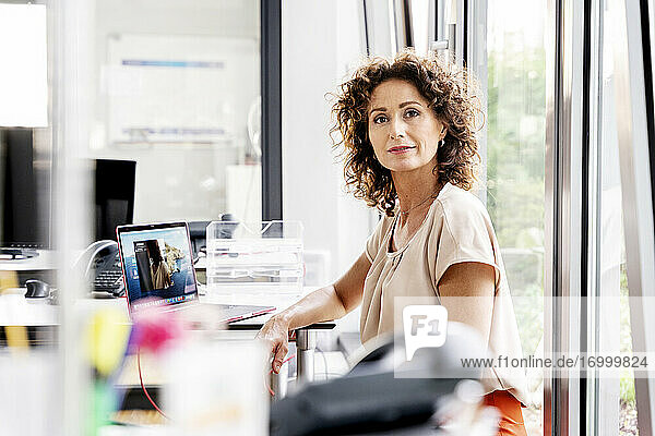 Confident businesswoman sitting by desk at office