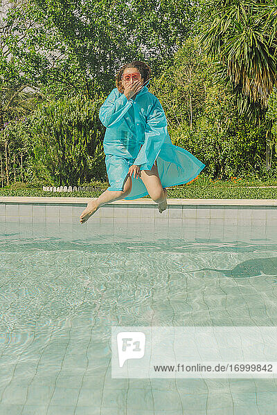 Woman in blue rain coat jumping into swimming pool