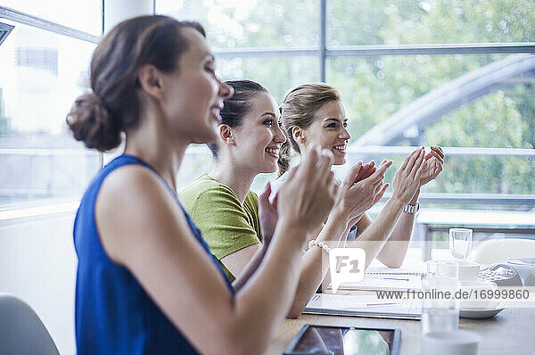 Happy female colleagues applauding while sitting in board room during meeting in office