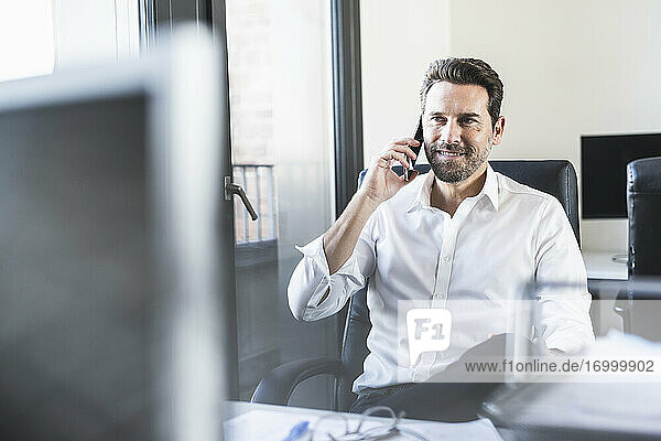 Älterer Geschäftsmann  der auf einem Stuhl im Büro sitzt und mit seinem Handy telefoniert