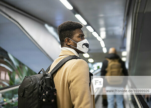 Young man wearing face mask standing on escalator at station