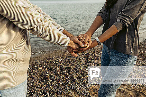 Freundin und Freund stapeln die Hände  während sie am Strand stehen