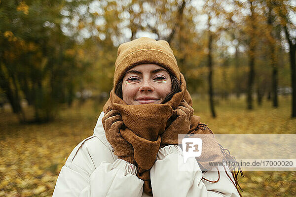 Lächelnde junge Frau  eingewickelt in einen Schal  im herbstlichen Park
