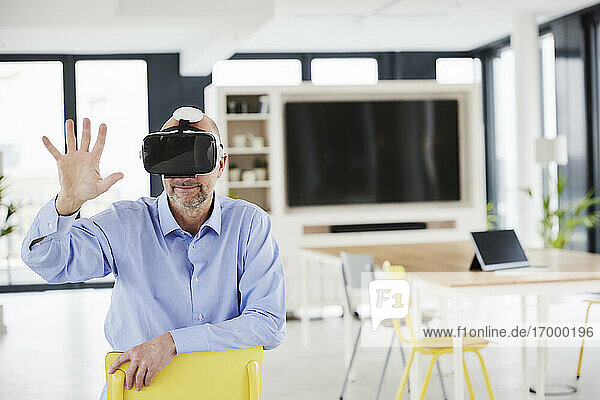 Geschäftsmann mit Virtual-Reality-Headset  der auf einem Stuhl sitzt und sich berührt
