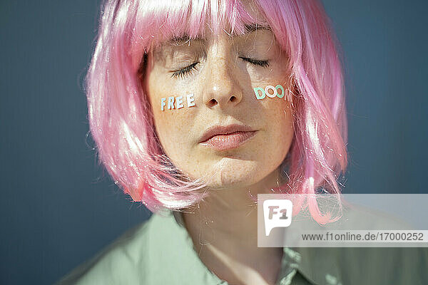 Junge Frau mit rosafarbener Perücke  Buchstaben im Gesicht  freiem Untergang  mit geschlossenen Augen