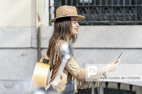 Junge Musikerin mit Elektroroller und Smartphone an der Wand