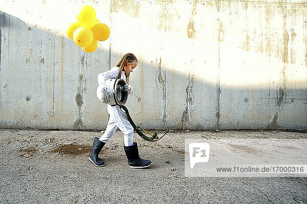Kleines Mädchen geht mit Weltraumhelm und hält Ballon auf der Straße während sonnigen Tag