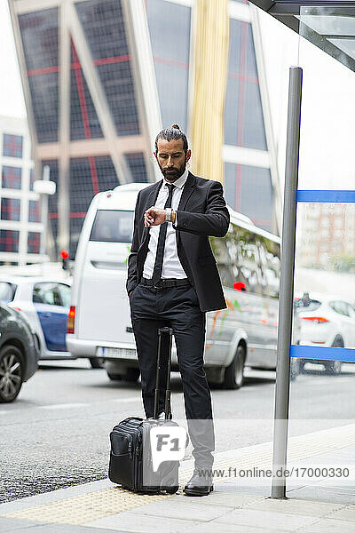Bearded businessman checking time while waiting at bus stop