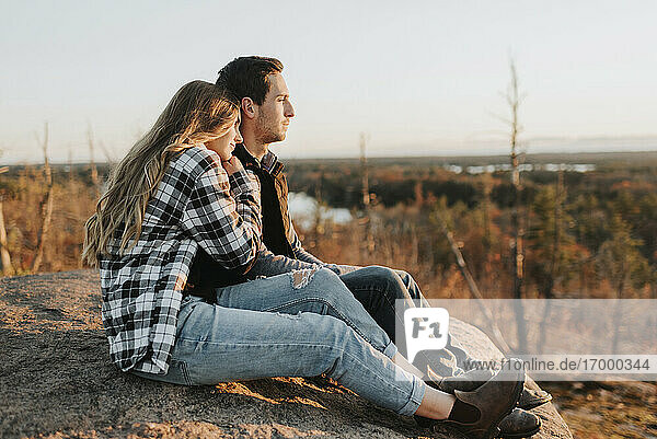 Junges Paar sitzt bei einer Herbstwanderung auf einem Felsen zusammen